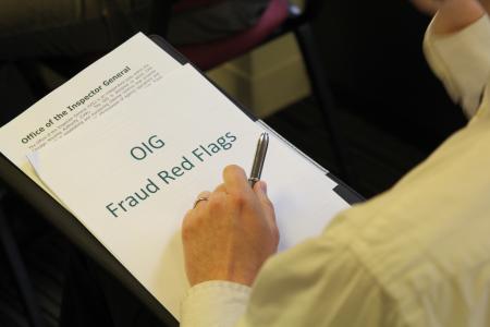A person holding a pen is reviewing a document titled "OIG Fraud Red Flags" on a clipboard. The document has the heading "Office of the Inspector General" and includes a brief description of the Office's role within the Chicago Housing Authority (CHA). The person is wearing a light-colored shirt, and only their hand and part of their arm are visible in the image. The setting appears to be a meeting or training session.
